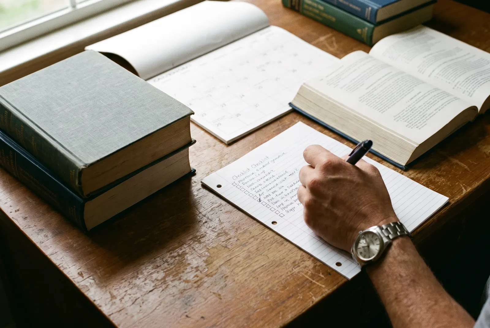 Accounting textbooks, a calendar and a handwritten checklist on a desk, planning CPA requirements step by step