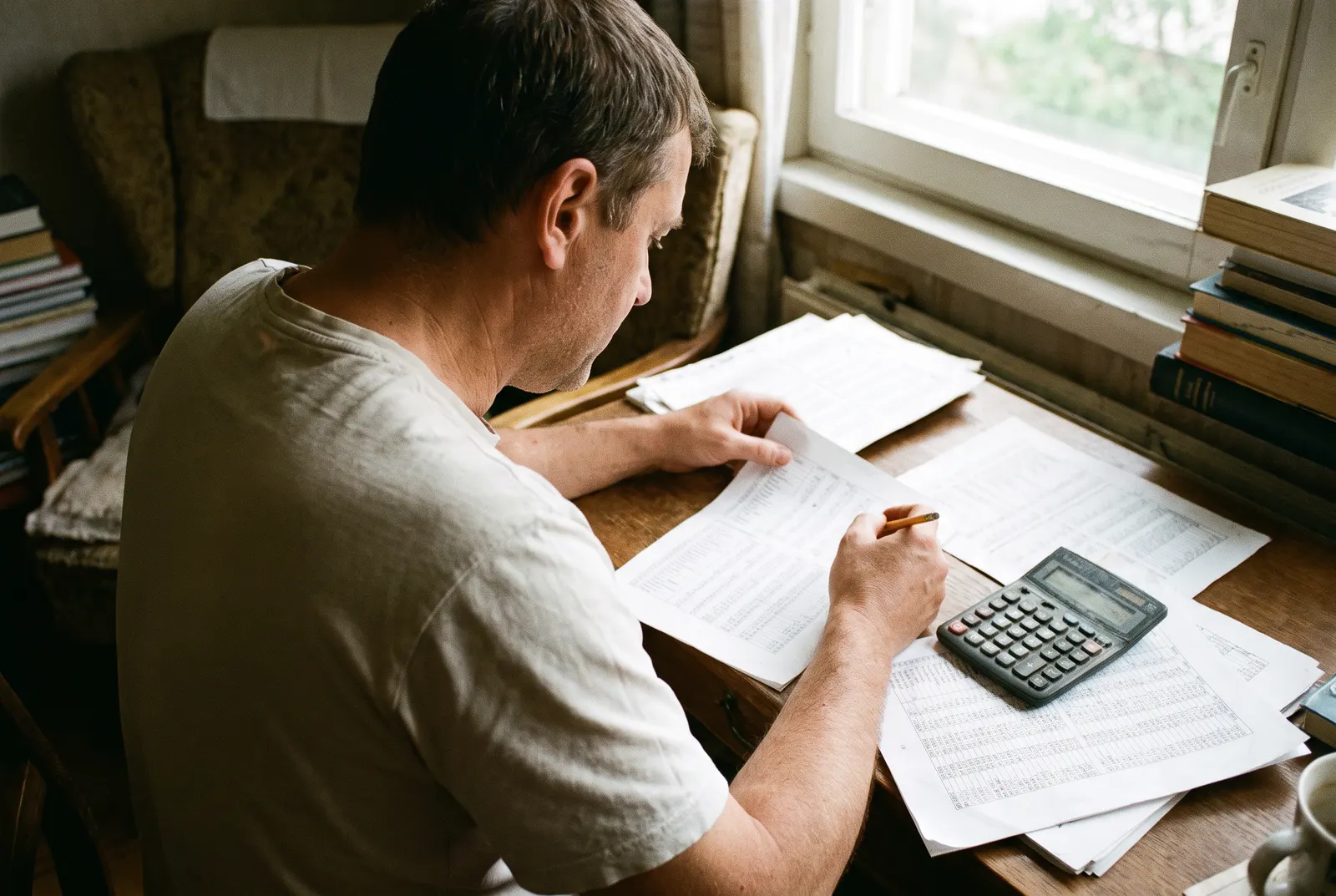 Man comparing printed tables of figures with a pencil and calculator at a desk, weighing accounting degree rankings
